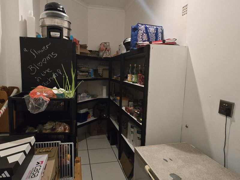 A functional walk-in pantry or scullery area featuring corner shelving and tiled flooring, providing ample storage space for kitchen essentials.