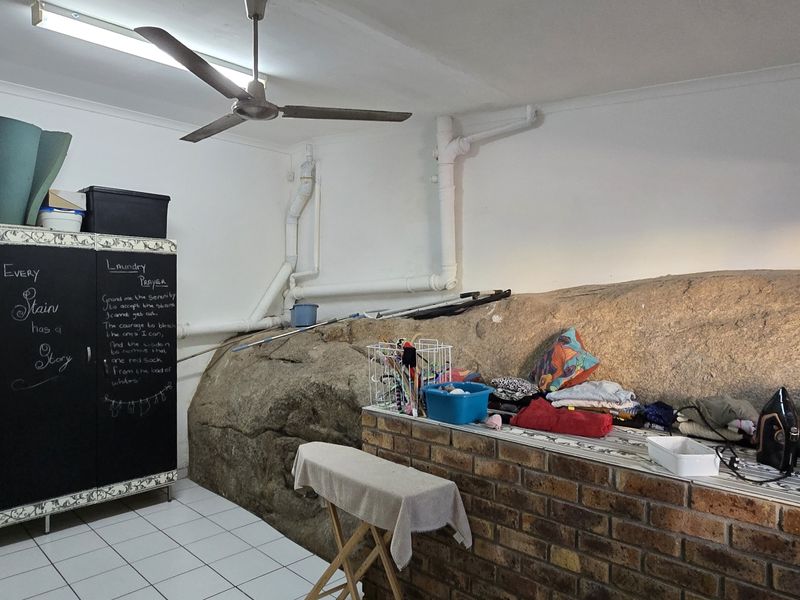 A functional laundry room featuring a unique natural rock wall, tiled flooring, ceiling fan, and built-in brick counter space.