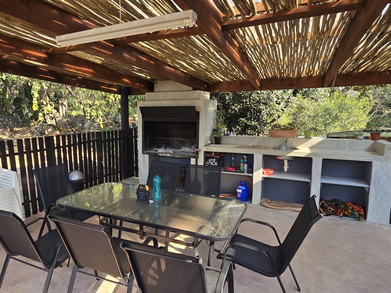 Covered outdoor patio featuring a built-in braai, concrete prep counter with sink, and a rustic timber-slatted roof structure.