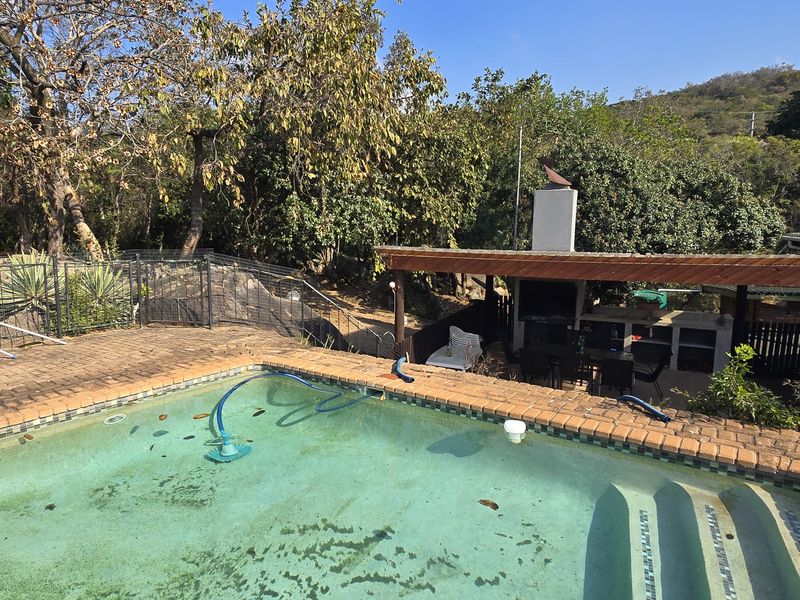 Outdoor entertainment area featuring a swimming pool with brick coping and a covered patio with a built-in braai fireplace.
