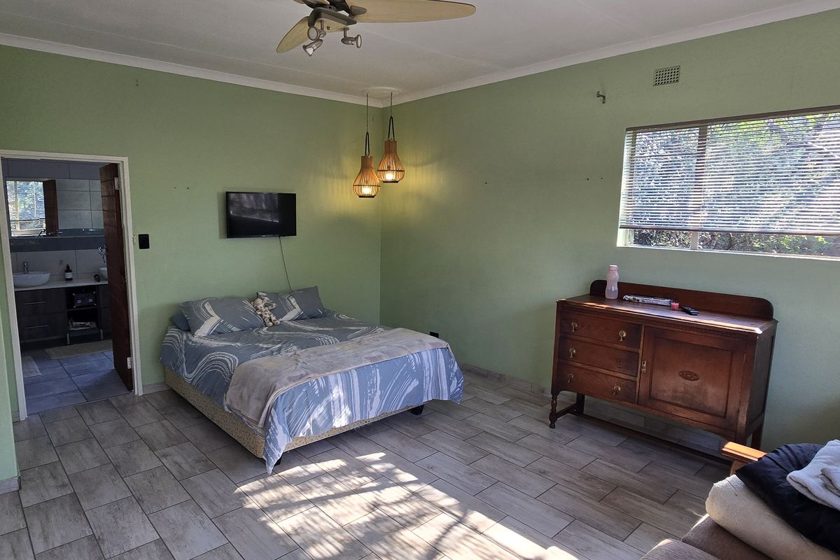 Spacious bedroom featuring tiled flooring, ceiling fan, and an en-suite bathroom access, offering a functional layout with natural light.