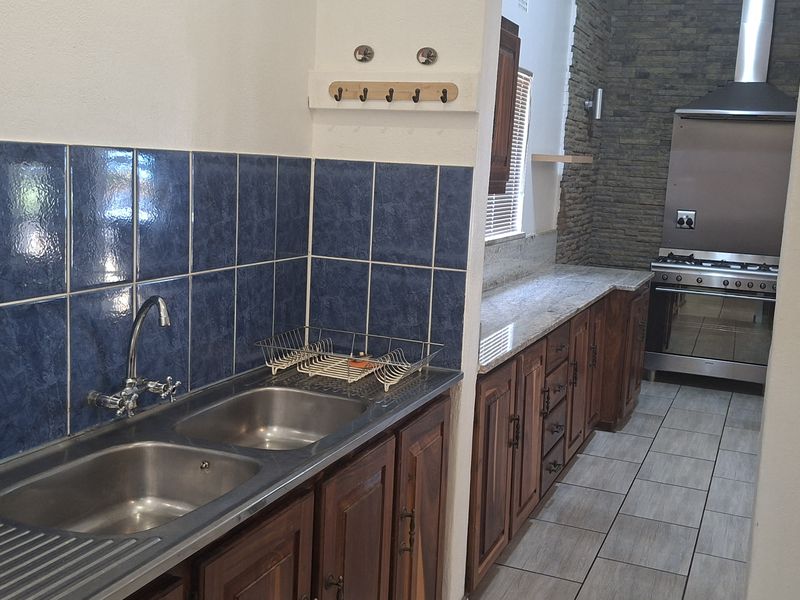 A functional kitchen featuring wooden cabinetry, stone countertops, a double sink, and a stainless steel gas stove with an extractor fan.