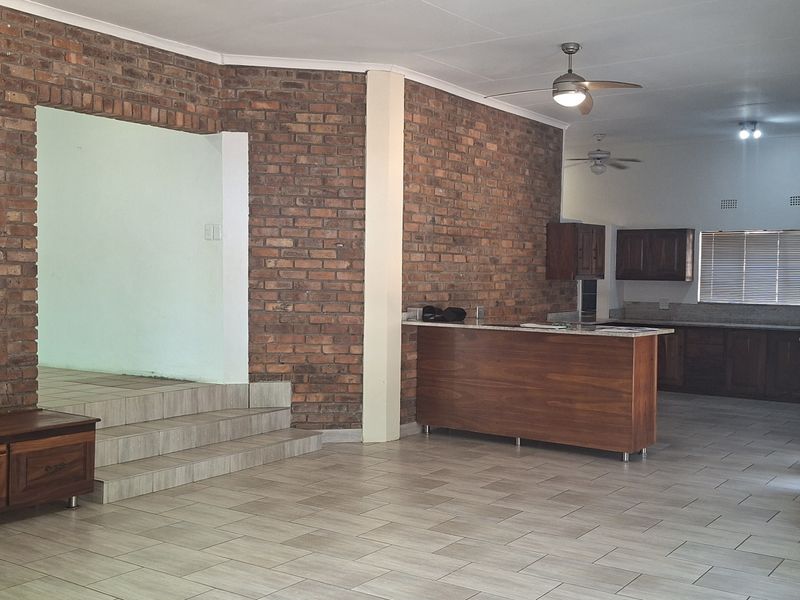 Spacious open-plan living and kitchen area featuring exposed brick walls, tiled flooring, a breakfast bar, and functional built-in cabinetry.