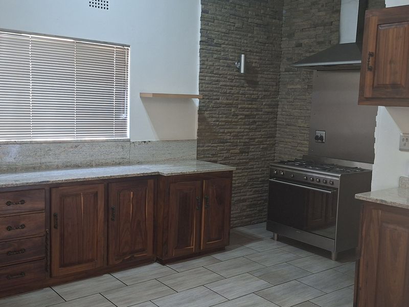 A functional kitchen featuring wooden cabinetry, granite countertops, a stone feature wall, and a stainless steel gas stove with an extractor fan.