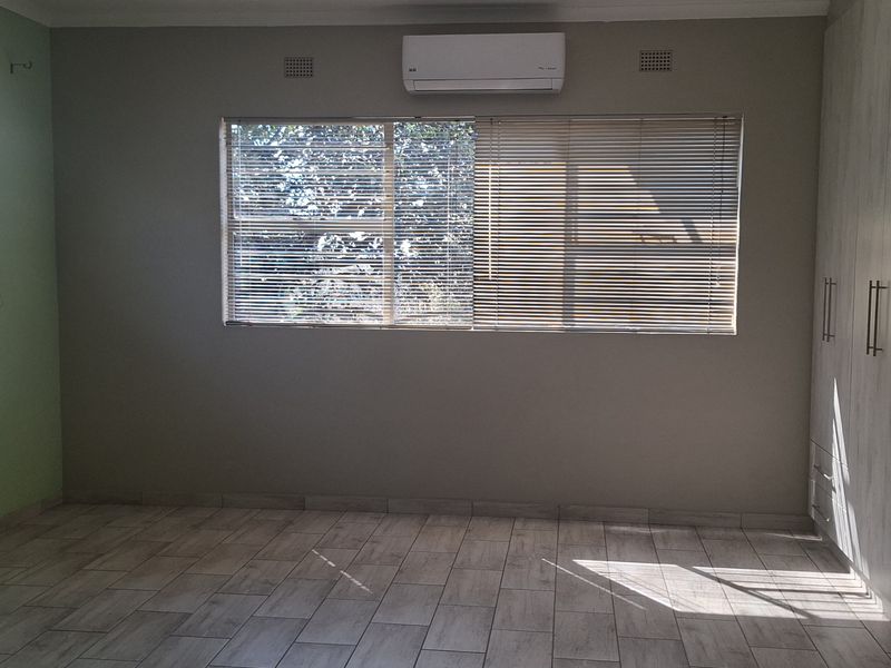 Spacious bedroom featuring neutral tiled flooring, extensive built-in cabinetry, and a wall-mounted air conditioning unit.