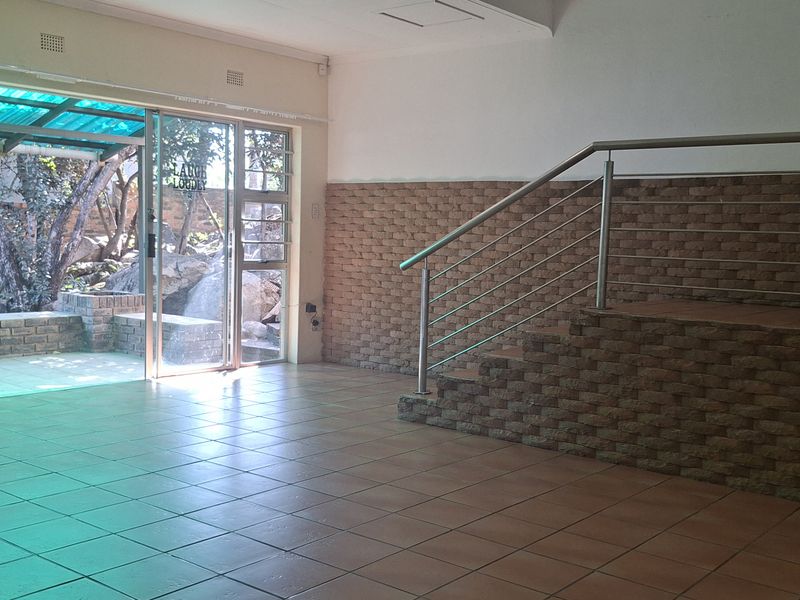 Spacious open-plan living area featuring tiled floors, a brick feature wall, and a staircase with stainless steel railings, leading to an outdoor patio area.