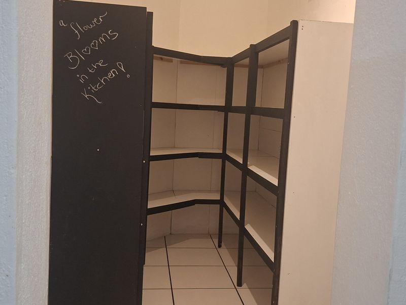 A functional walk-in pantry or scullery area featuring built-in shelving and tiled flooring, providing ample storage space.
