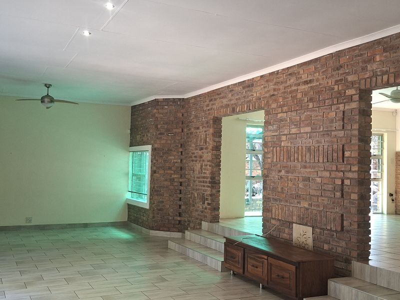 Spacious open-plan living area featuring exposed brick walls, tiled flooring, and a split-level layout with an integrated staircase.