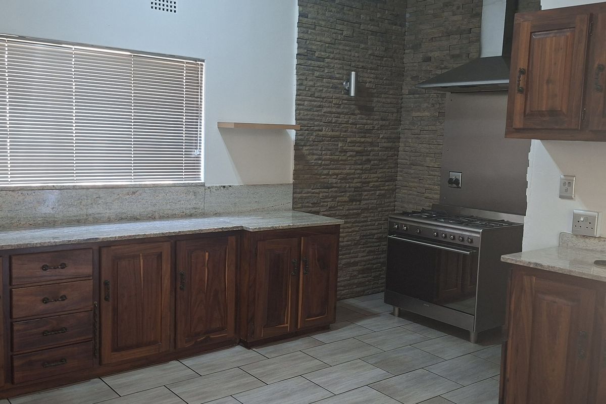 A functional kitchen featuring wooden cabinetry, granite countertops, a stone feature wall, and a stainless steel gas stove with an extractor fan.