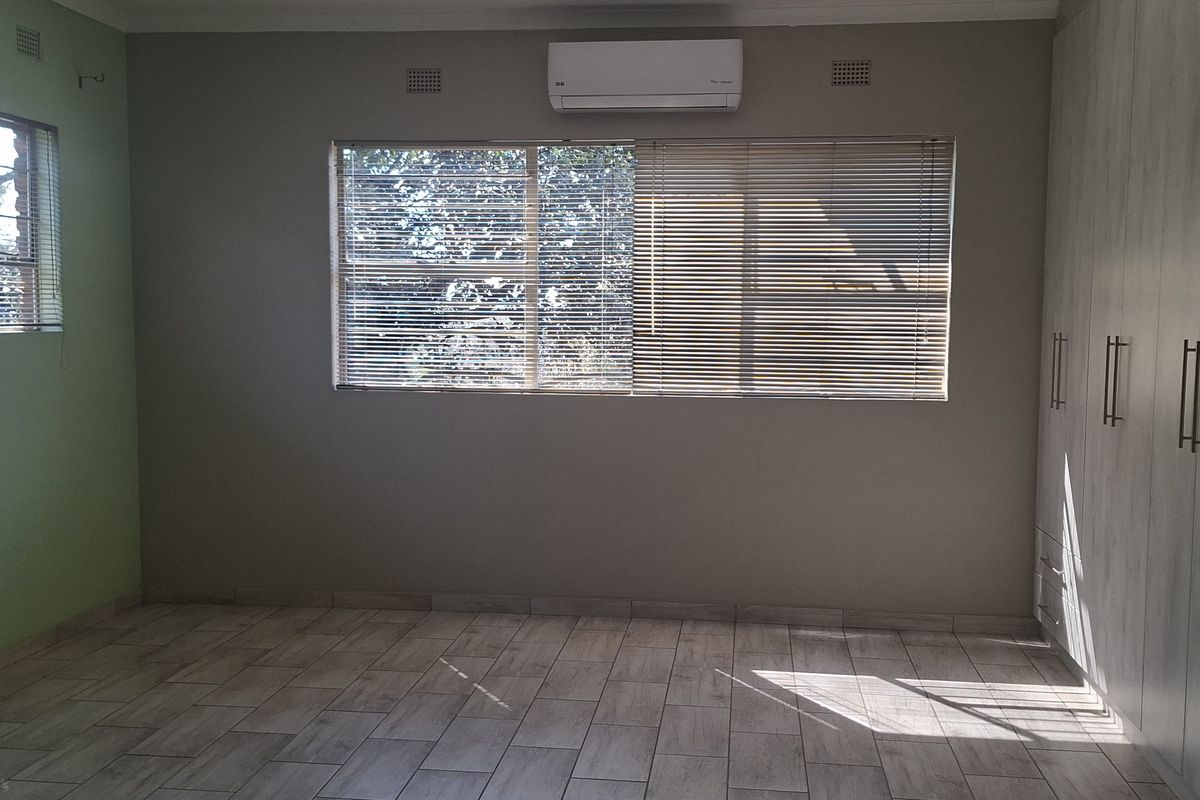 Spacious bedroom featuring neutral tiled flooring, extensive built-in cabinetry, and a wall-mounted air conditioning unit.