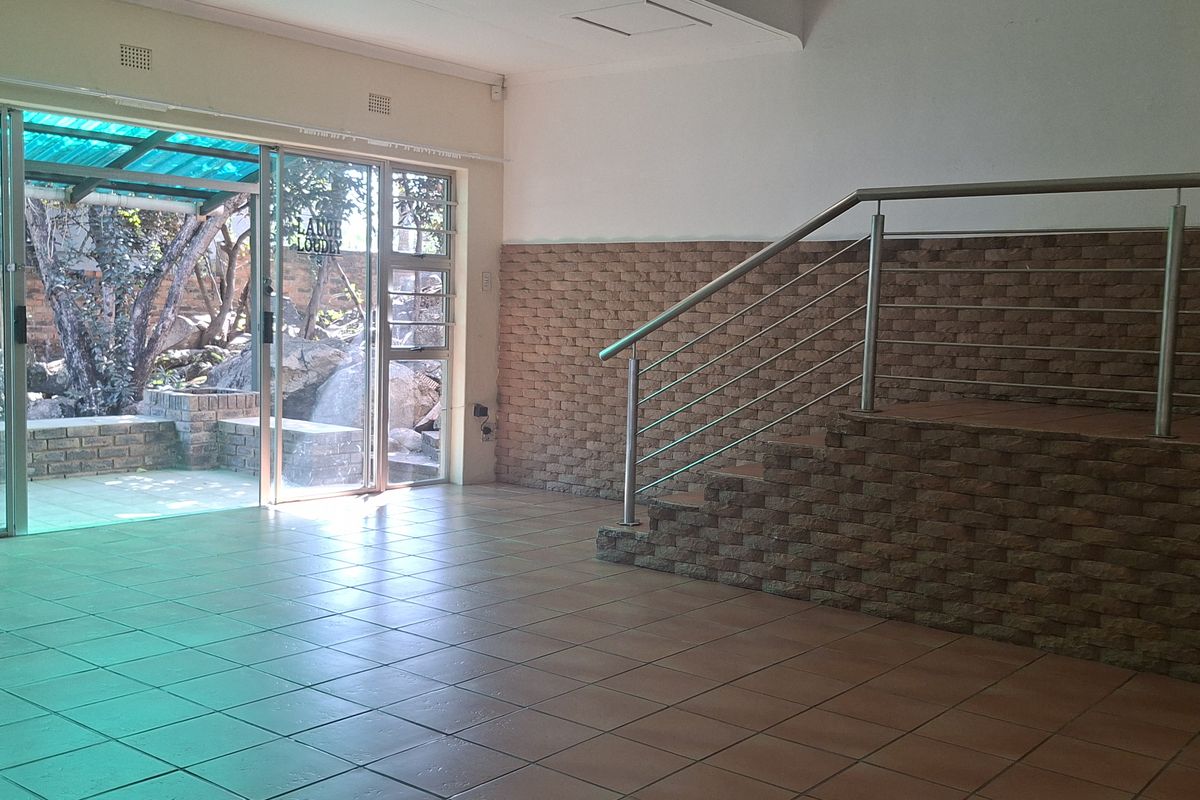 Spacious open-plan living area featuring tiled floors, a brick feature wall, and a staircase with stainless steel railings, leading to an outdoor patio area.