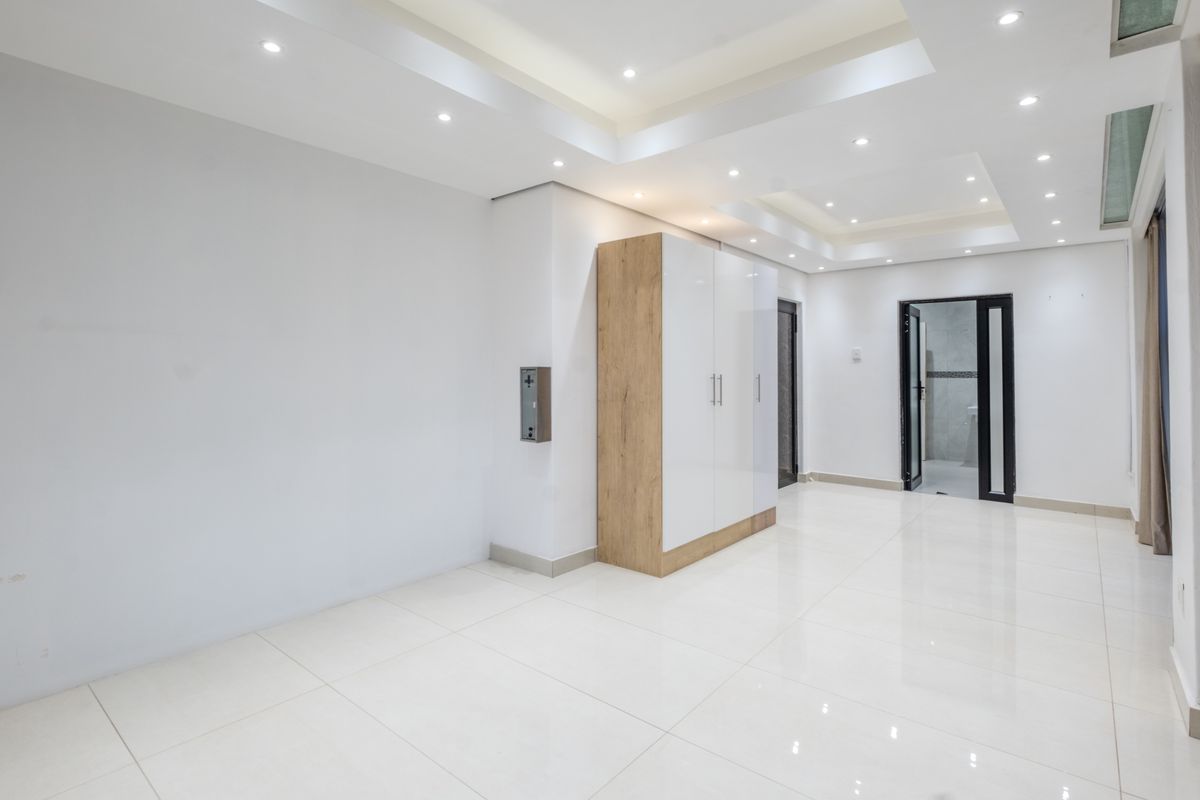 A bright, modern bedroom featuring a tray ceiling with recessed lighting, high-gloss tiled floors, and a sleek built-in wardrobe.