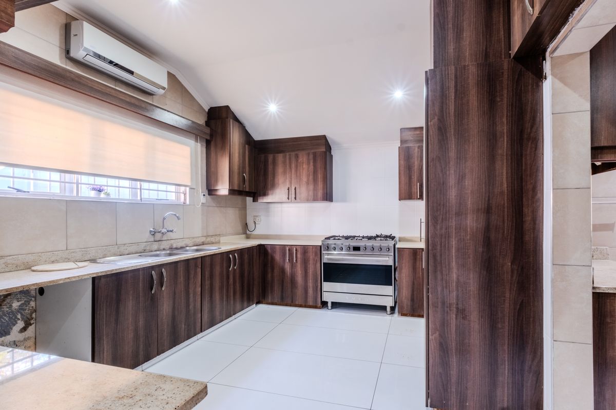 A modern kitchen featuring dark wood cabinetry, stone countertops, a gas stove with oven, and tiled flooring, offering a clean and functional workspace.