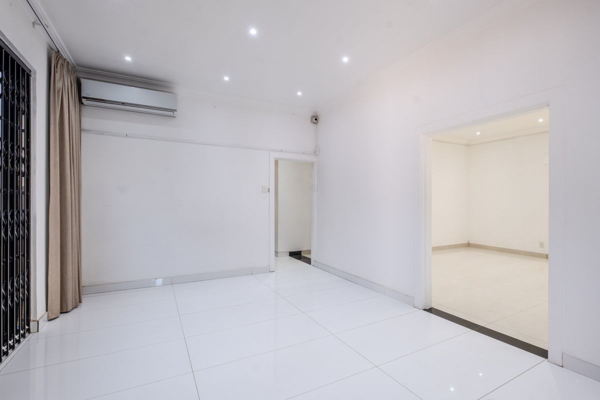 A bright, empty living area featuring white tiled flooring, recessed downlighting, and a wall-mounted split-system air conditioner.