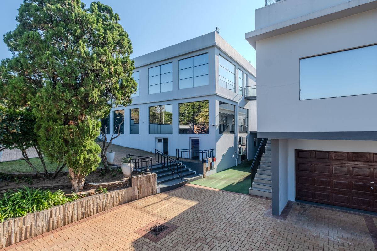 Rear exterior view of a modern multi-story property featuring large glass windows, paved driveway, and external staircase access.
