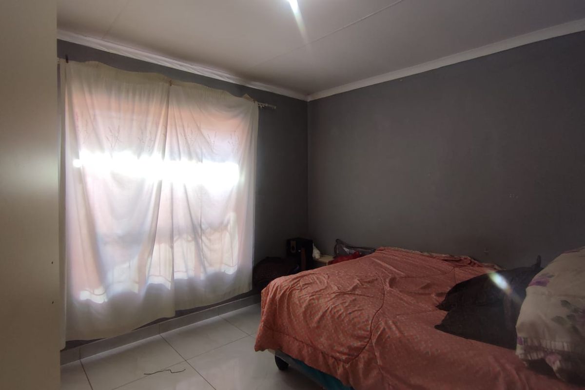 A bedroom featuring tiled flooring and neutral wall tones, offering a functional space that could benefit from cosmetic updates and improved lighting.