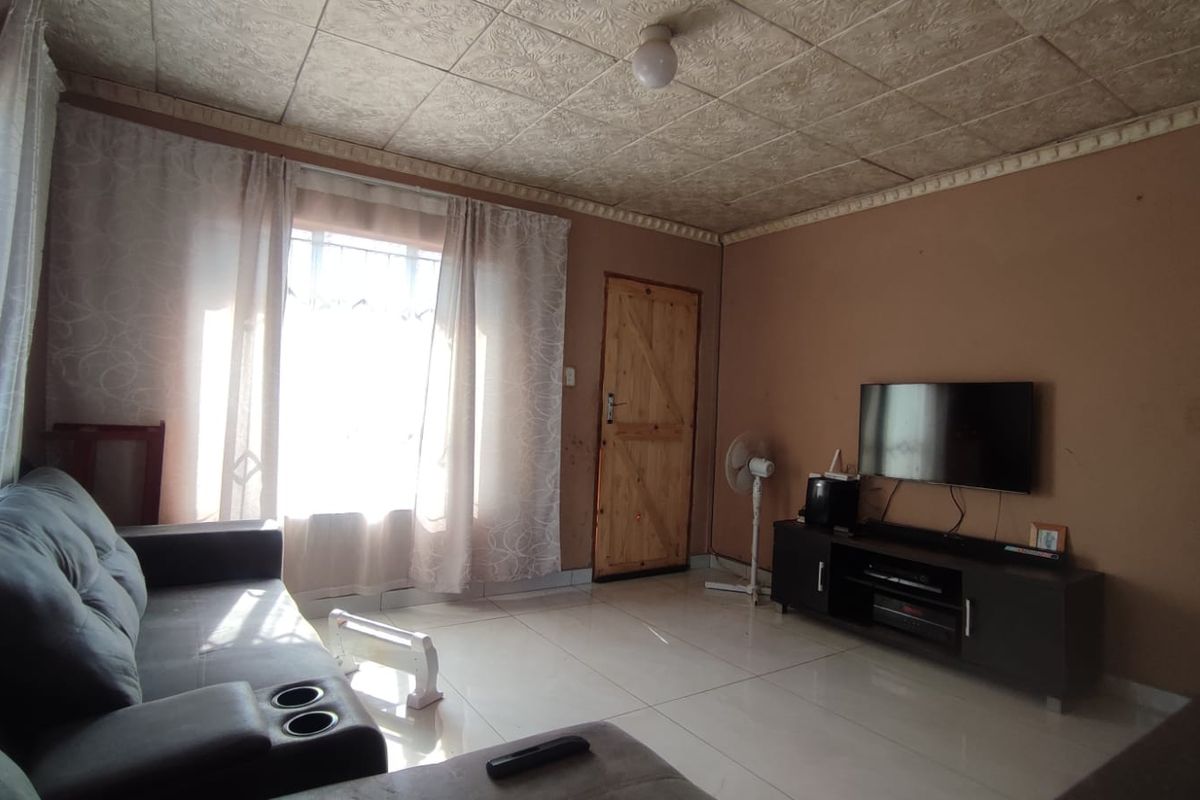 A living room featuring tiled flooring, a textured ceiling, and a timber door, offering a functional space with potential for cosmetic updates.