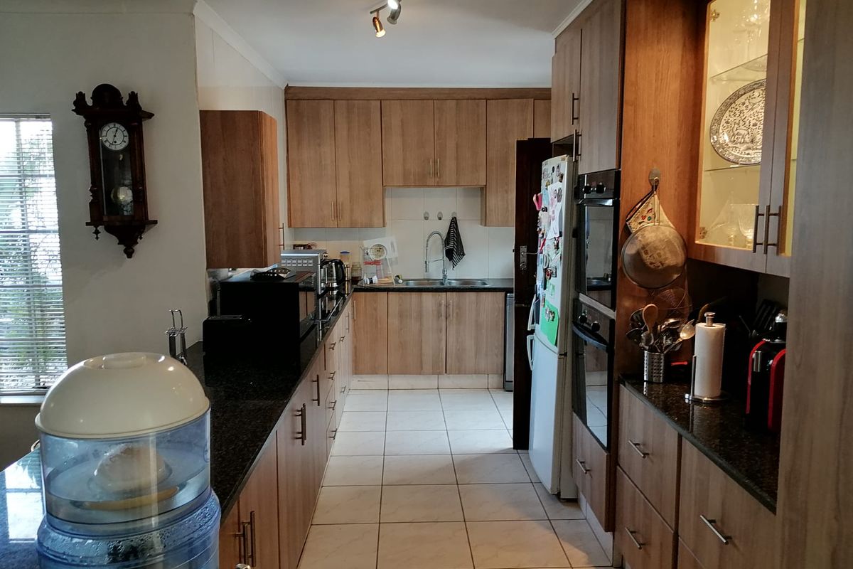 A functional kitchen featuring wood-finish cabinetry, granite countertops, a double wall oven, and tiled flooring with ample storage space.
