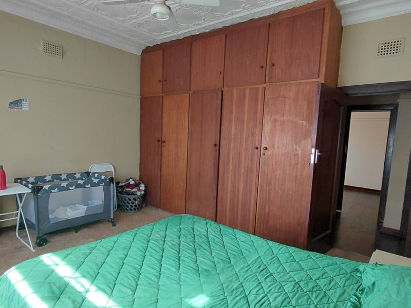 A bedroom featuring a large built-in timber wardrobe and an ornate plaster ceiling with a central ceiling fan.