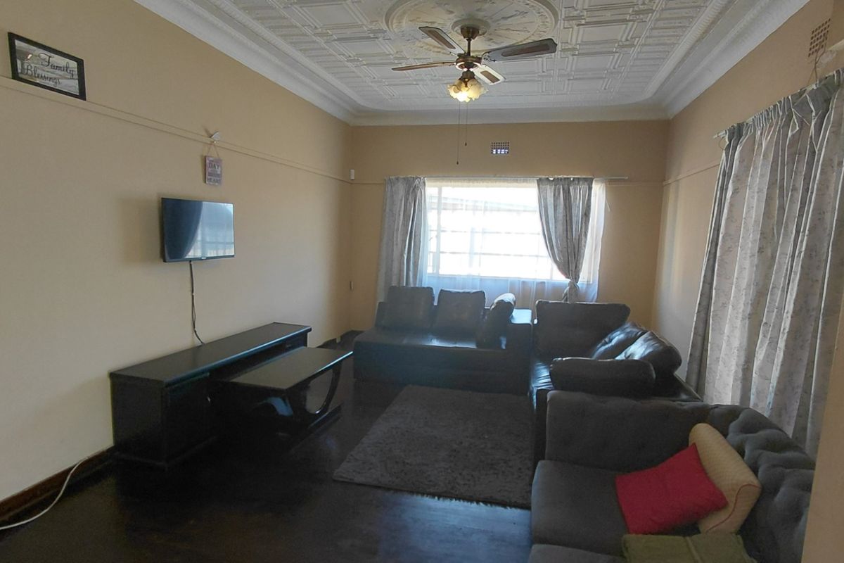 A spacious living room featuring classic ornate pressed metal ceilings, a ceiling fan, and dark timber flooring, offering a traditional aesthetic.