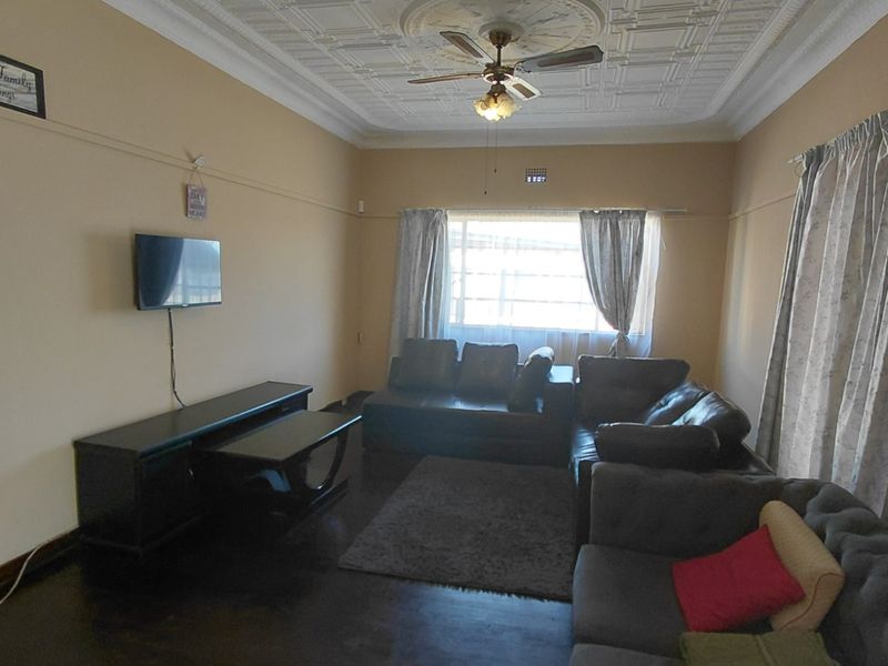 A spacious living room featuring classic ornate pressed metal ceilings, a ceiling fan, and dark timber flooring, offering a traditional aesthetic.