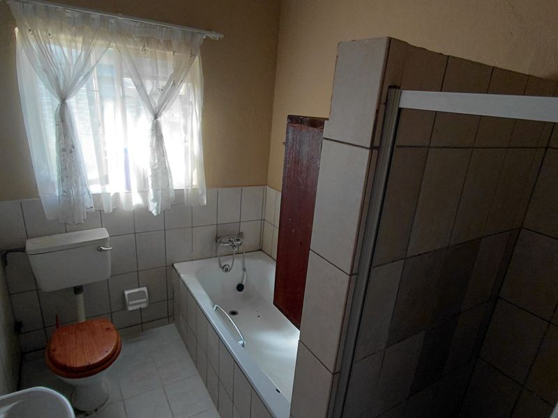 A functional bathroom featuring a bathtub, separate shower enclosure, and toilet with neutral wall tiling.