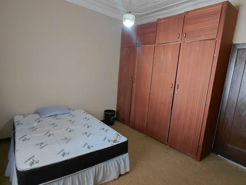 A bedroom featuring built-in wooden cupboards and decorative ceiling cornicing, requiring updates to flooring and finishes to modernize the space.