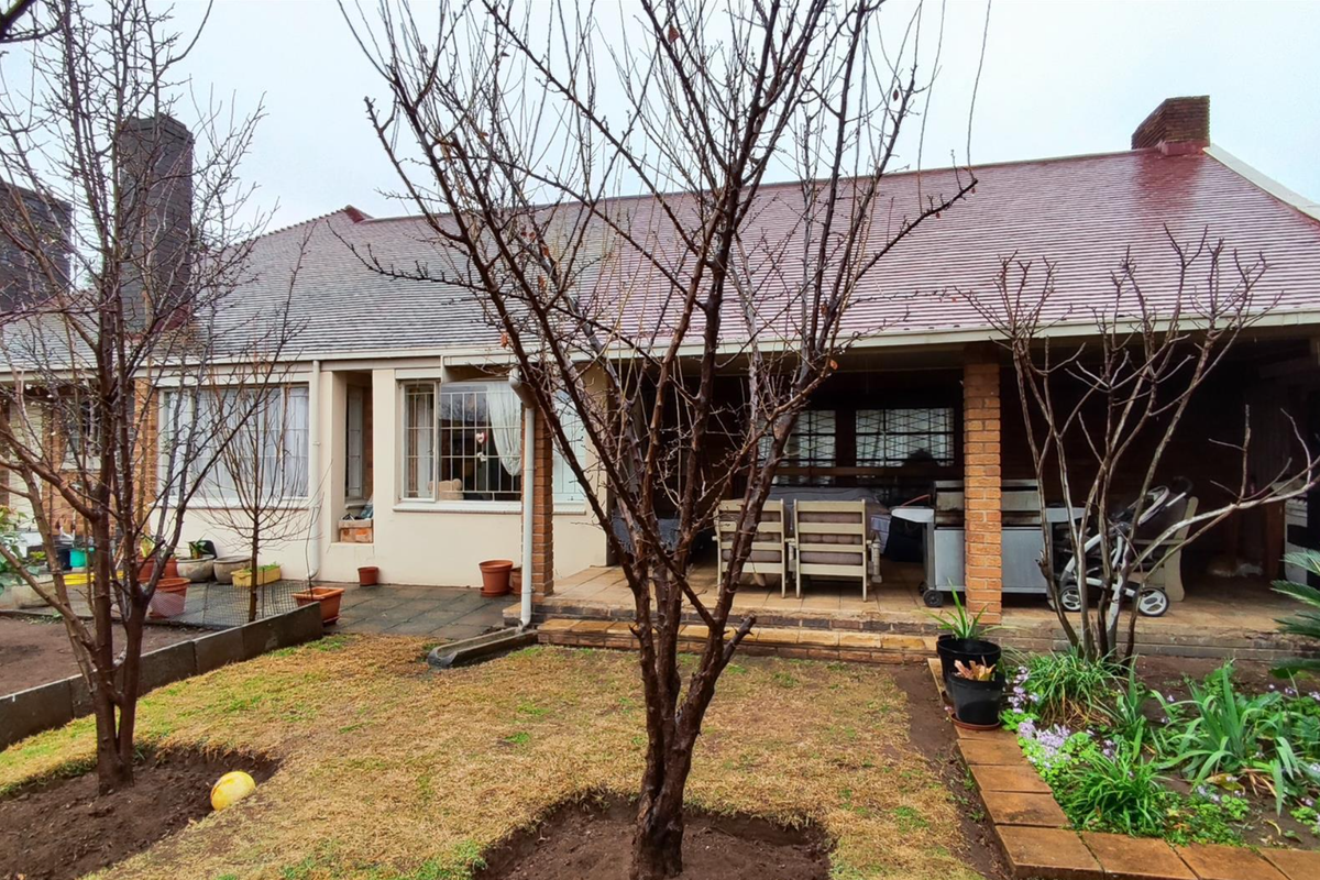 Rear view of the house featuring a covered patio area, brick pillars, and a garden with established trees.