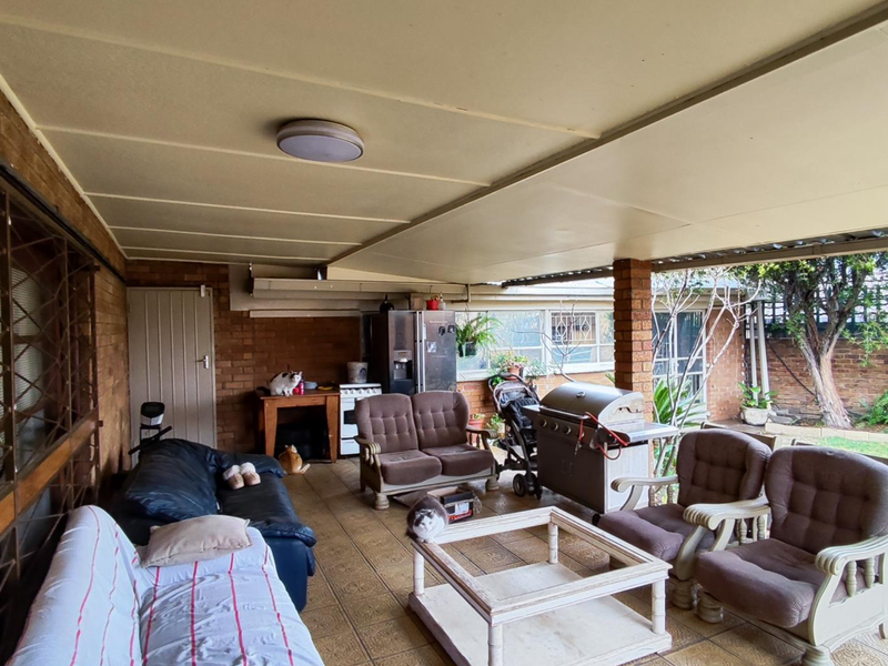 A spacious covered patio area featuring brick walls, tiled flooring, and direct access to the rear garden.