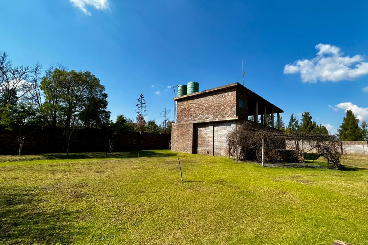 Rear view of a face brick building on a small holding, featuring water storage tanks, a perimeter wall, and a garden area with a pergola.