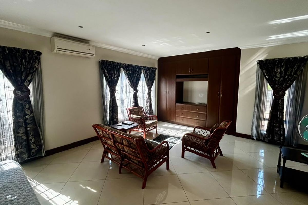 Spacious living room featuring large format floor tiles, built-in wooden cabinetry, and a wall-mounted air conditioning unit.