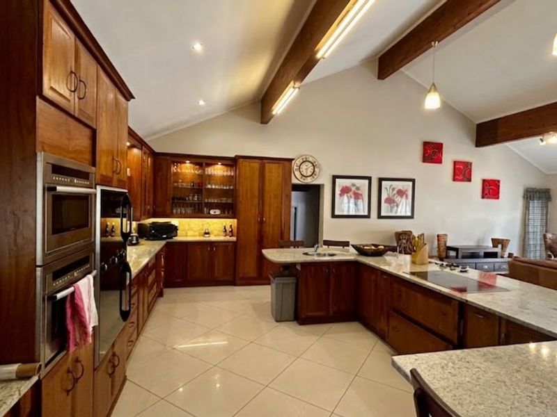 Spacious open-plan kitchen featuring warm timber cabinetry, stone countertops, integrated appliances, and high vaulted ceilings with exposed wooden beams.