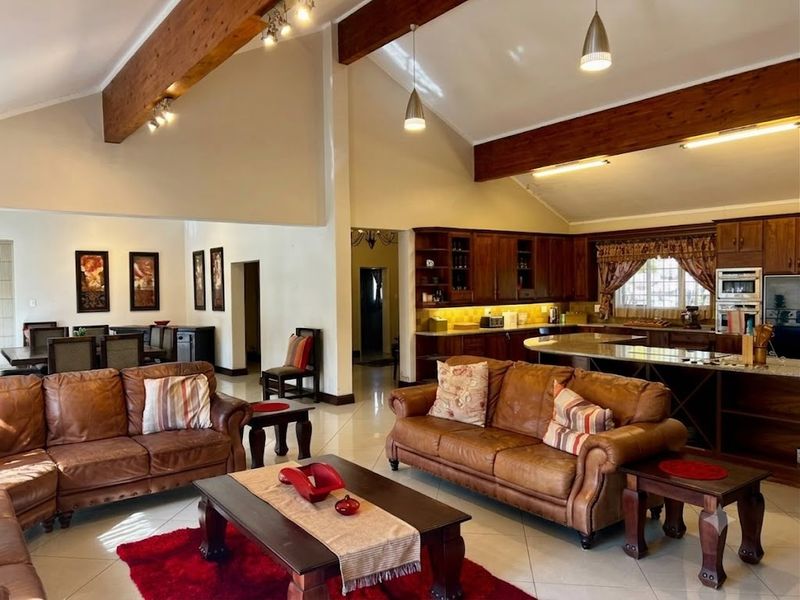 Spacious open-plan living area featuring vaulted ceilings with exposed timber beams, tiled flooring, and a well-appointed kitchen with wooden cabinetry and granite countertops.
