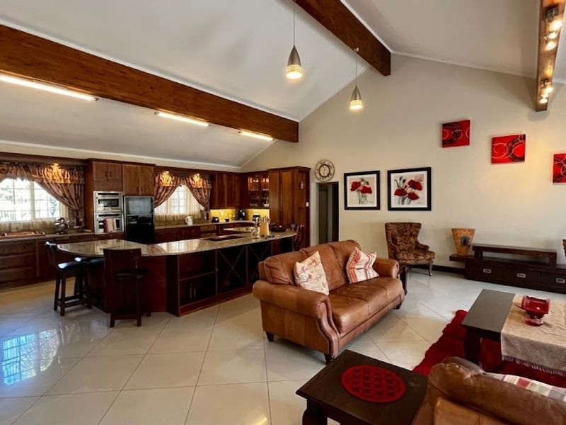 Spacious open-plan living area featuring a large kitchen with granite countertops, an island, and striking exposed timber beams under a high vaulted ceiling.