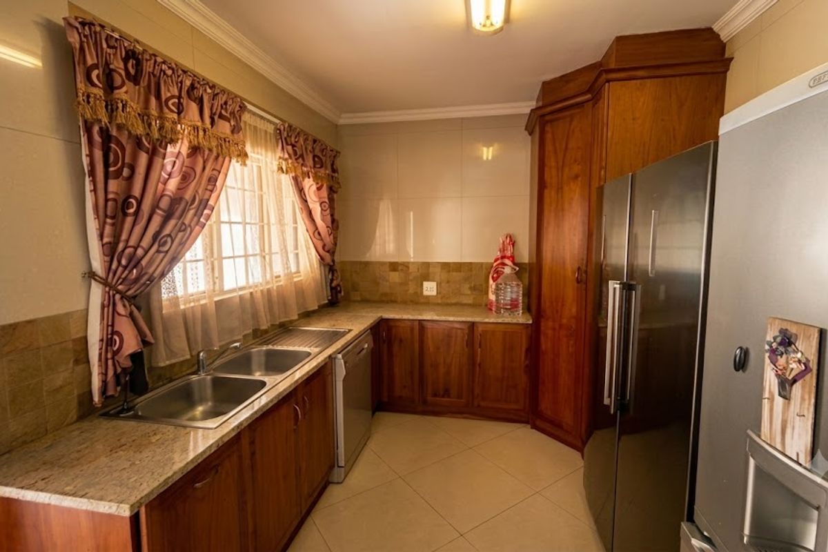 A functional kitchen featuring warm wooden cabinetry, granite countertops, a double basin sink, and neutral tiled flooring with a classic backsplash.