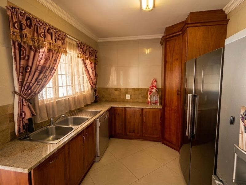 A functional kitchen featuring warm wooden cabinetry, granite countertops, a double basin sink, and neutral tiled flooring with a classic backsplash.