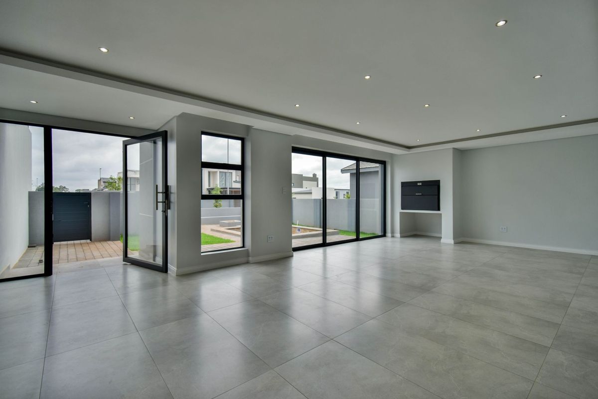 Spacious, modern open-plan living area featuring large format floor tiles, recessed lighting, and seamless access to the outdoor patio through sliding doors.