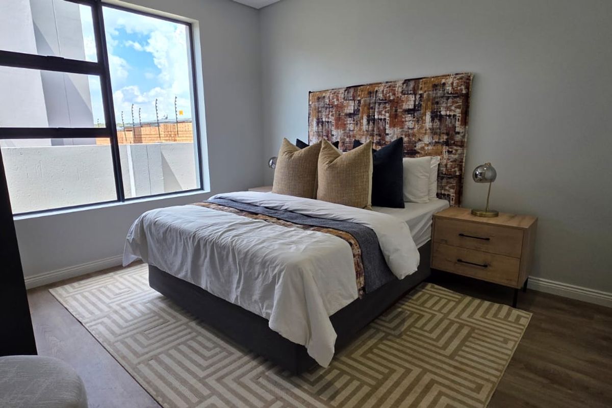A well-maintained bedroom featuring modern laminate flooring, neutral wall finishes, and a large window providing natural light.