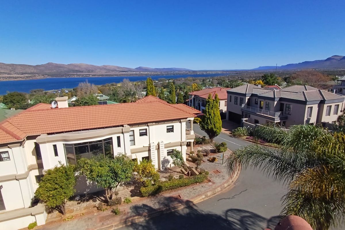 An elevated aerial view of the property showcasing the roof structure, surrounding neighborhood, and scenic lake and mountain landscape in the background.