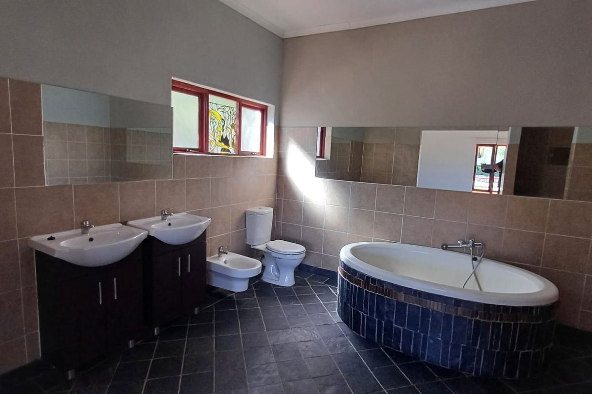 Spacious bathroom featuring a double vanity, bidet, toilet, and a tiled freestanding bathtub with dark stone accents and large wall-mounted mirrors.