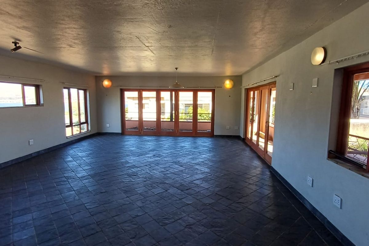 Spacious, empty living area featuring dark slate tile flooring, large wooden-framed folding doors, and ample natural light with views.