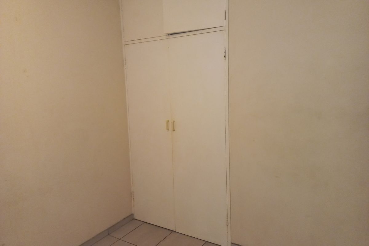 An empty bedroom featuring tiled flooring and a built-in cupboard with overhead storage, requiring minor cosmetic updates to the wall finishes.