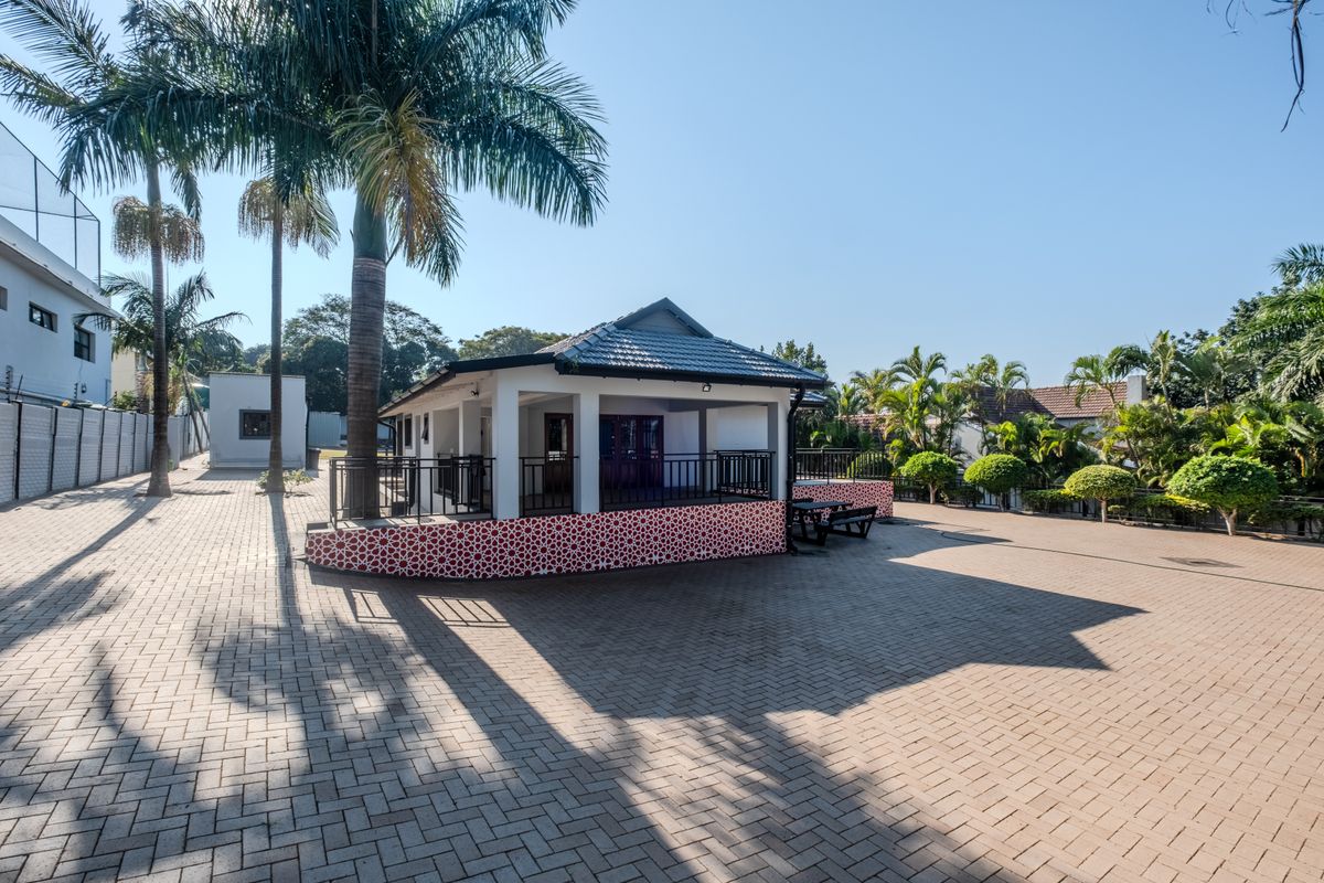 A spacious paved rear courtyard featuring a covered patio area with decorative tile accents and metal railings, surrounded by established palm trees.