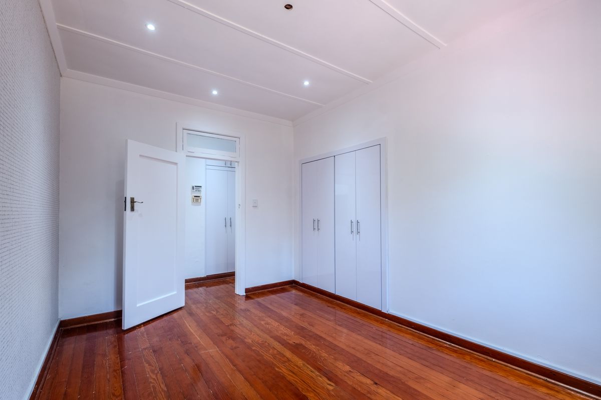 A bright, empty bedroom featuring polished hardwood flooring, built-in white cupboards, and modern recessed ceiling lighting.