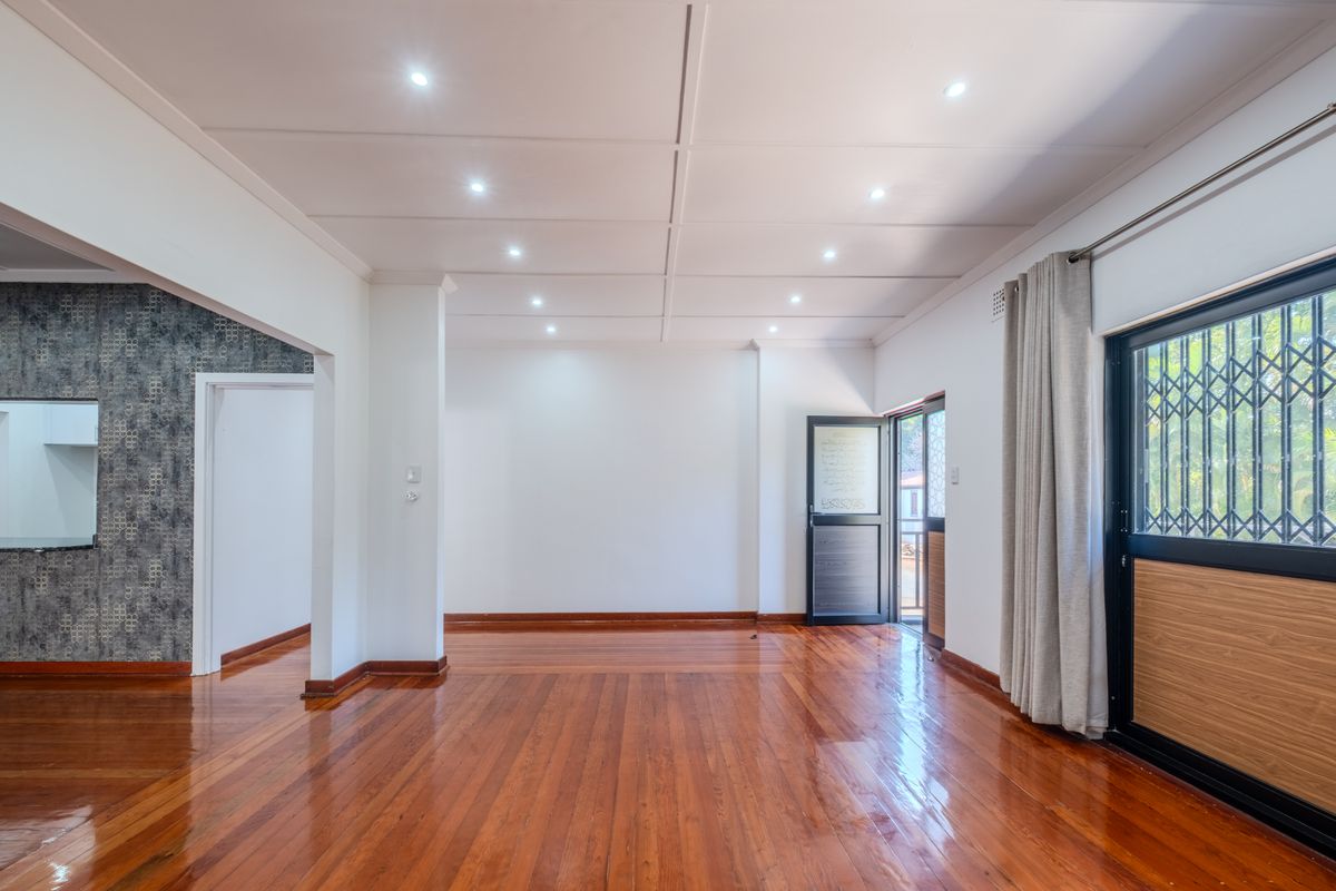 Spacious, light-filled living area featuring polished hardwood flooring, recessed ceiling lighting, and a sliding glass door with security gate access to the exterior.