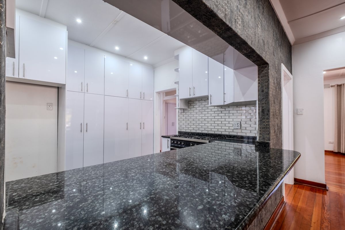 Modern kitchen featuring white cabinetry, granite countertops, subway tile backsplash, and gas stove, with a breakfast bar overlooking the adjacent living area.