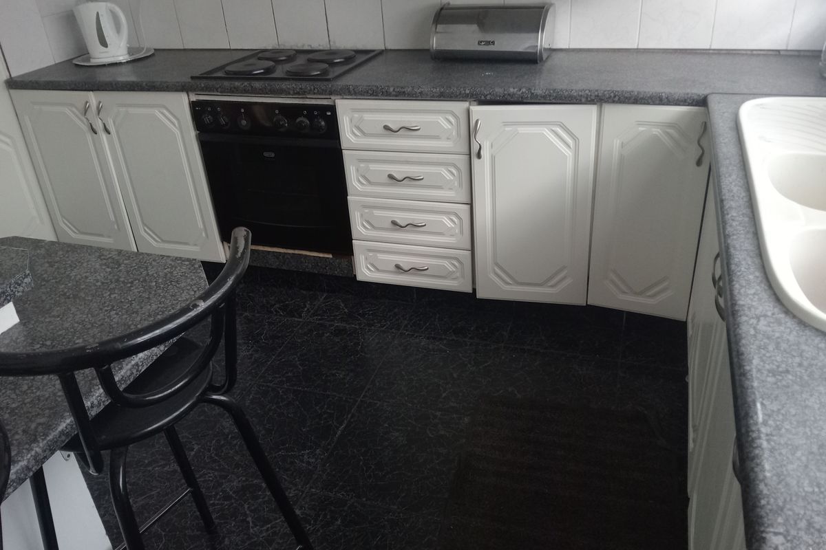 A functional kitchen featuring white cabinetry, dark laminate countertops, a built-in oven with electric hob, and a double basin sink.