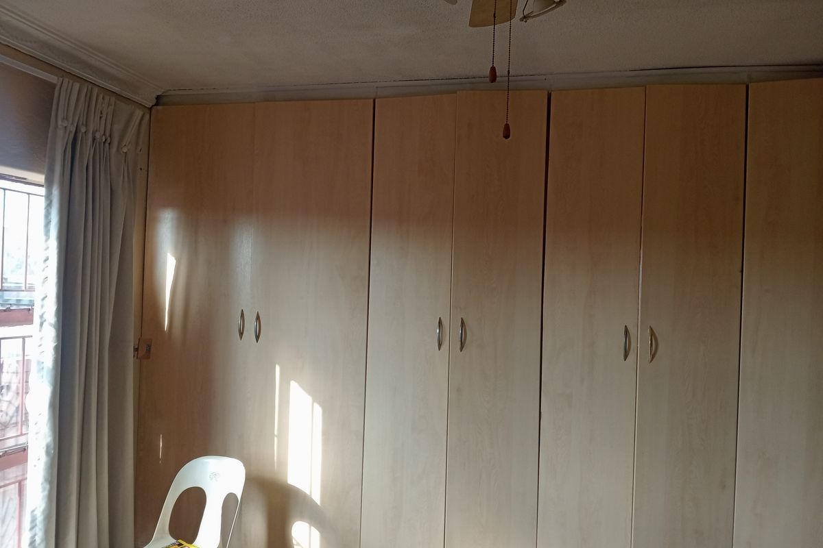 A bedroom featuring extensive built-in wooden cupboards and a ceiling fan, requiring minor cosmetic attention to the ceiling finishes.