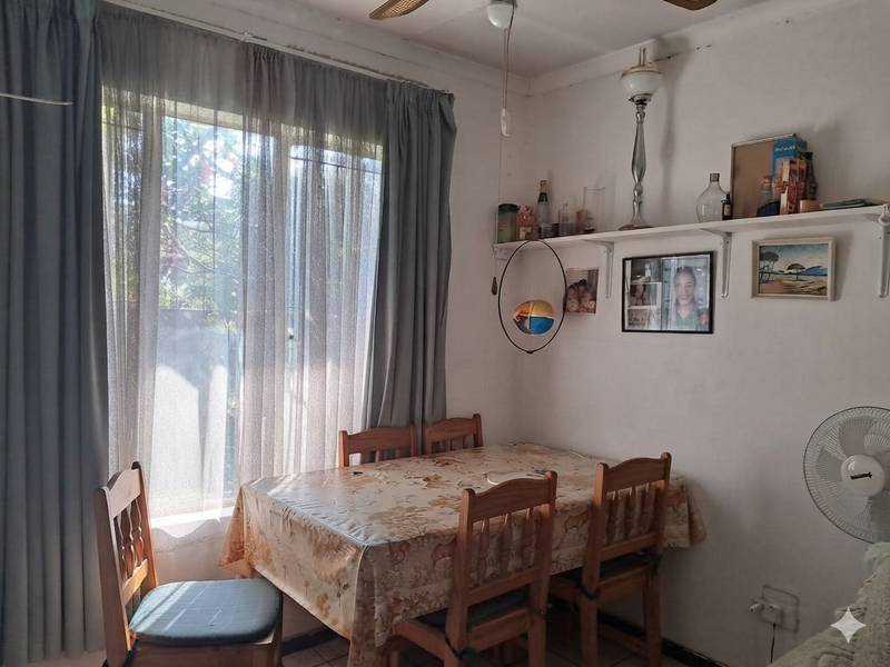 A dining area featuring a large sliding window with curtains, ceiling fan, and wall-mounted shelving, offering a functional space for meals.