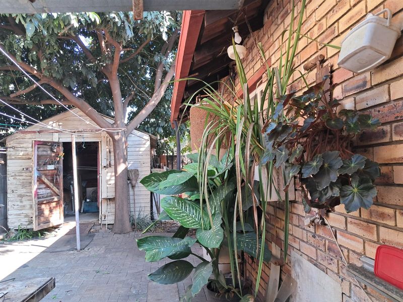 Rear exterior view featuring a paved patio area, brick wall facade, and a detached wooden storage shed under mature trees.